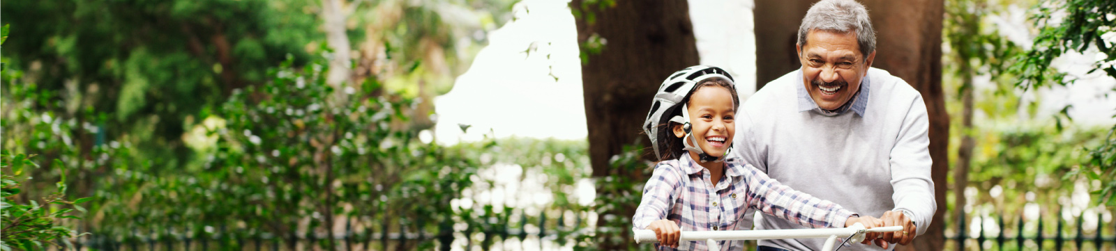 A grandfather teaching his granddaughter how to ride a bike